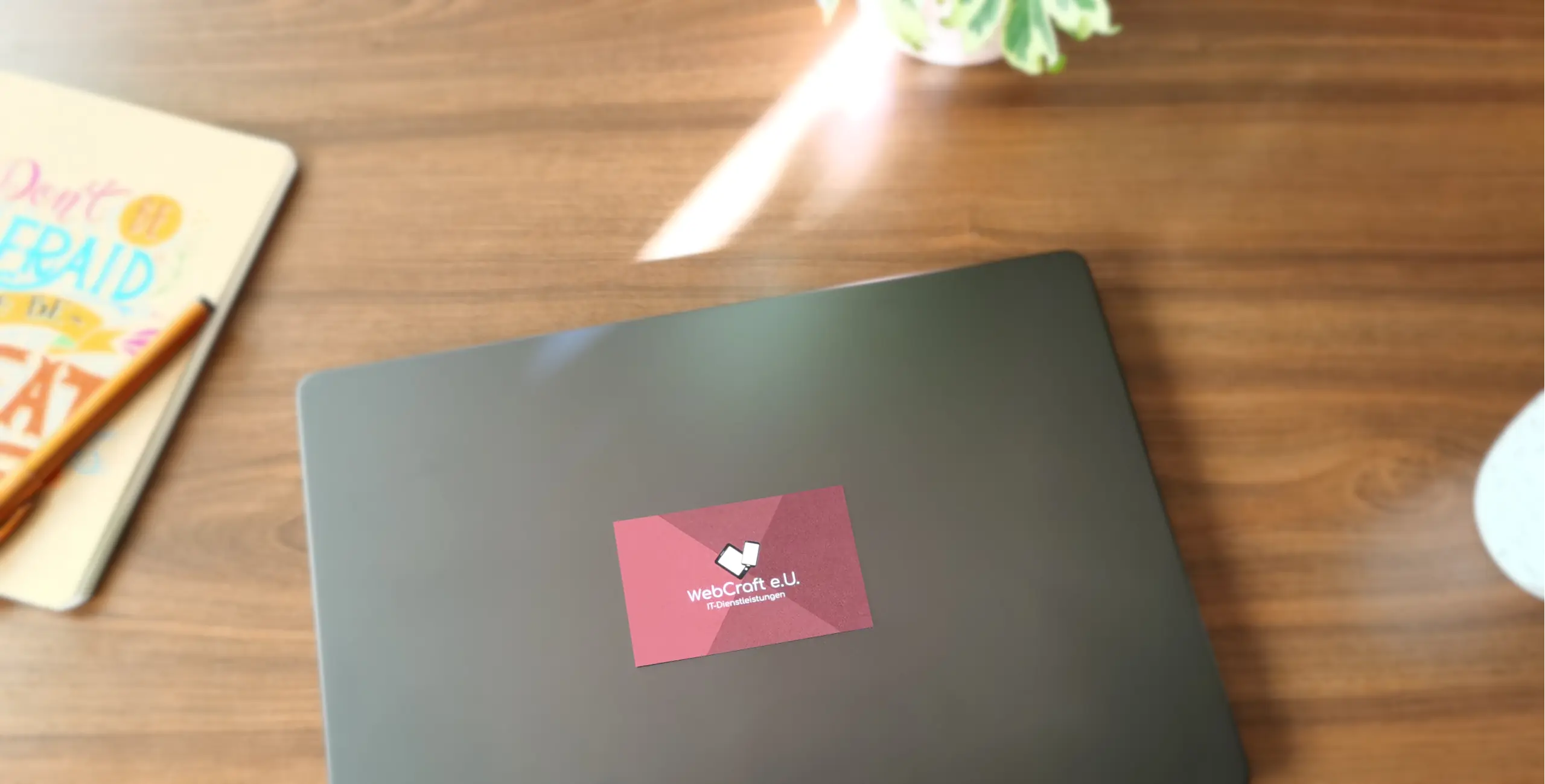 Geschäftskarte im Vordergrund, umgeben von verschwommenem Laptop, Kaffeetasse, Pflanze und Notizbuch – Symbol für digitale Zusammenarbeit und professionelle Beratung.